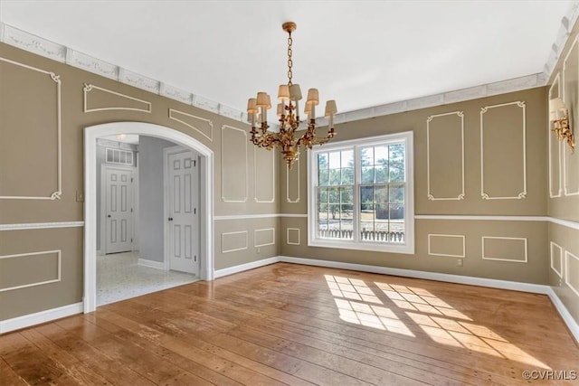 unfurnished dining area with arched walkways, light wood-style flooring, baseboards, and an inviting chandelier