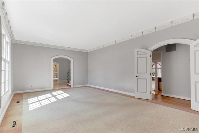 unfurnished room with light carpet, visible vents, arched walkways, and baseboards