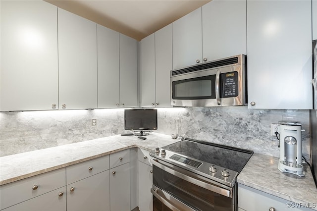 kitchen featuring tasteful backsplash, light stone counters, white cabinets, and appliances with stainless steel finishes