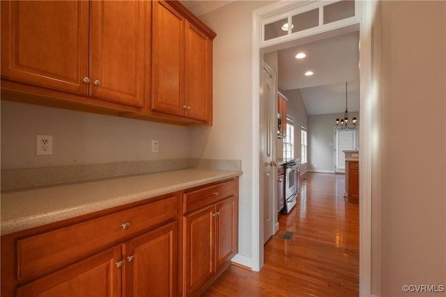 kitchen featuring an inviting chandelier, vaulted ceiling, light hardwood / wood-style flooring, pendant lighting, and oven