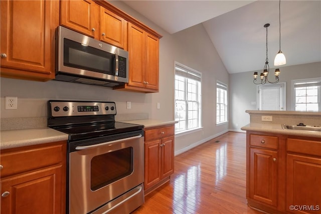 kitchen with lofted ceiling, stainless steel appliances, a notable chandelier, light hardwood / wood-style floors, and decorative light fixtures