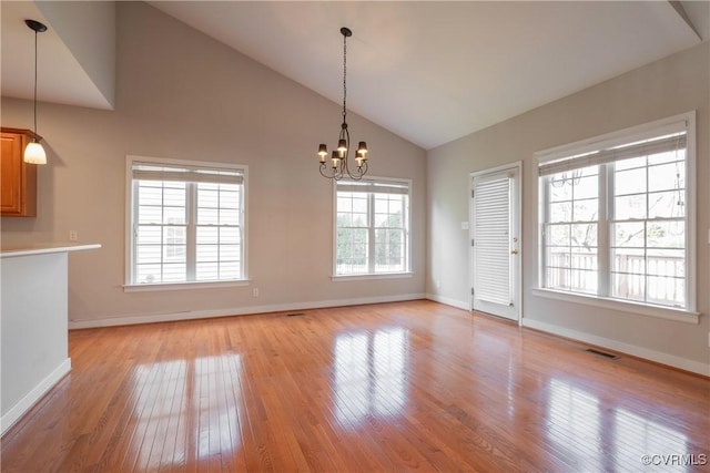 unfurnished dining area with high vaulted ceiling, a notable chandelier, and light wood-type flooring