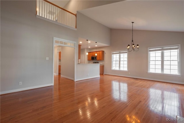 unfurnished living room with an inviting chandelier, high vaulted ceiling, and light wood-type flooring