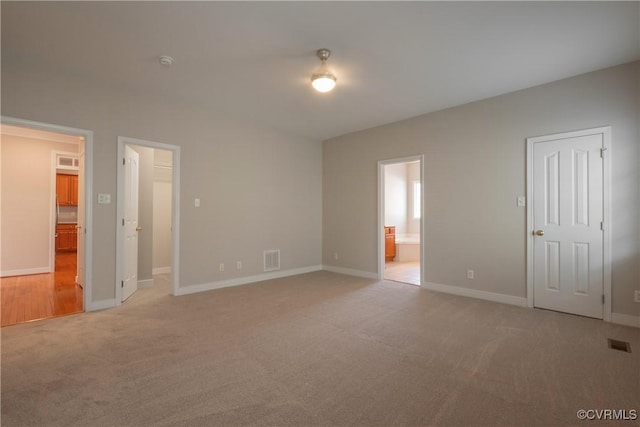 unfurnished bedroom with ensuite bathroom and light colored carpet