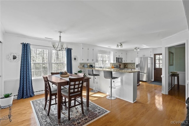 dining room featuring an inviting chandelier, ornamental molding, a wealth of natural light, and light hardwood / wood-style floors