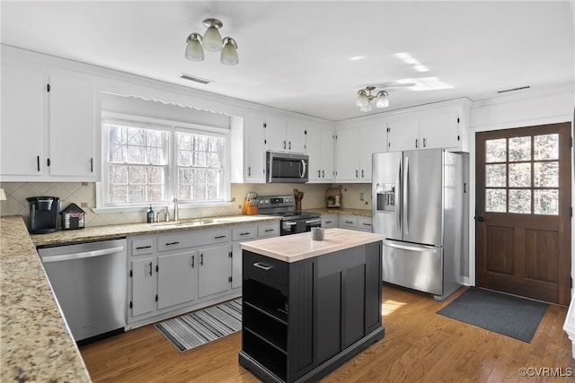 kitchen with stainless steel appliances, white cabinetry, hardwood / wood-style flooring, and light stone counters