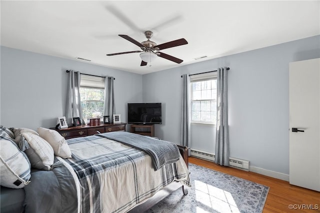 bedroom with multiple windows, a baseboard radiator, ceiling fan, and light hardwood / wood-style flooring