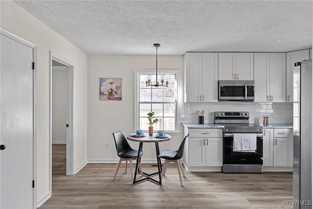 kitchen with tasteful backsplash, light hardwood / wood-style flooring, appliances with stainless steel finishes, pendant lighting, and white cabinets