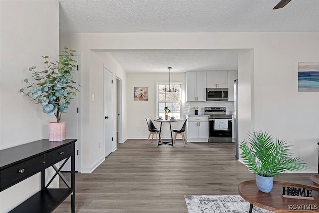 kitchen featuring appliances with stainless steel finishes, hardwood / wood-style floors, a textured ceiling, white cabinets, and decorative light fixtures