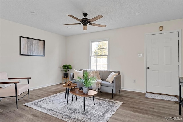 living room with hardwood / wood-style flooring, ceiling fan, and a textured ceiling