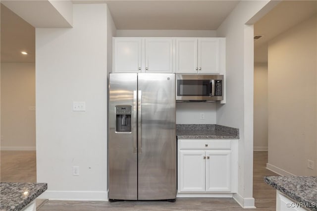 kitchen featuring white cabinets, appliances with stainless steel finishes, light hardwood / wood-style floors, and dark stone counters