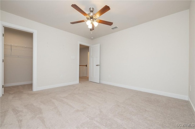 unfurnished bedroom featuring a spacious closet, light colored carpet, a closet, and ceiling fan