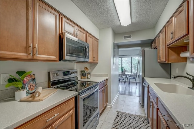 kitchen featuring sink, light tile patterned floors, stainless steel appliances, and a textured ceiling