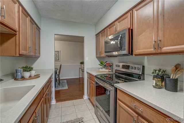 kitchen featuring appliances with stainless steel finishes, sink, light tile patterned floors, and a textured ceiling