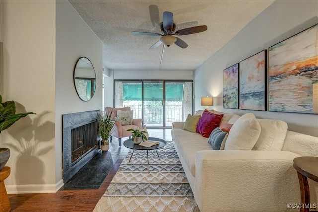 living room with ceiling fan, dark wood-type flooring, a premium fireplace, and a textured ceiling