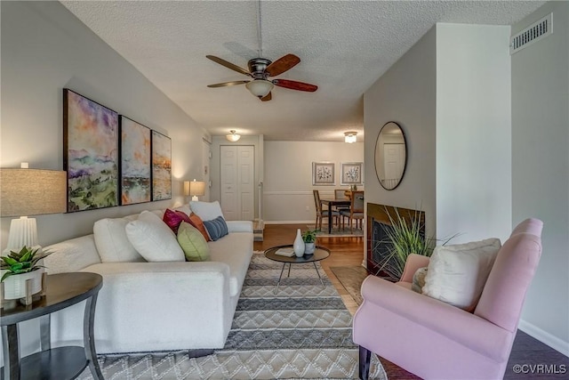 living room with wood-type flooring, ceiling fan, and a textured ceiling