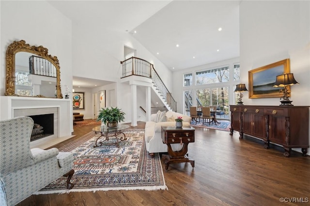 living room with recessed lighting, a high ceiling, wood finished floors, a fireplace with flush hearth, and stairs