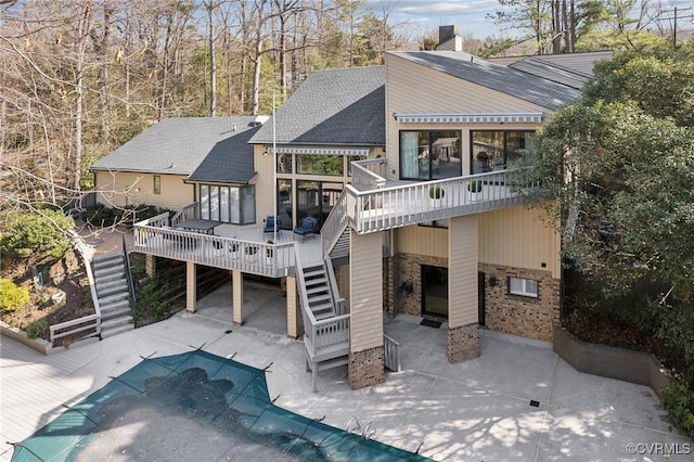 rear view of property with a shingled roof, stairway, a wooden deck, and a covered pool