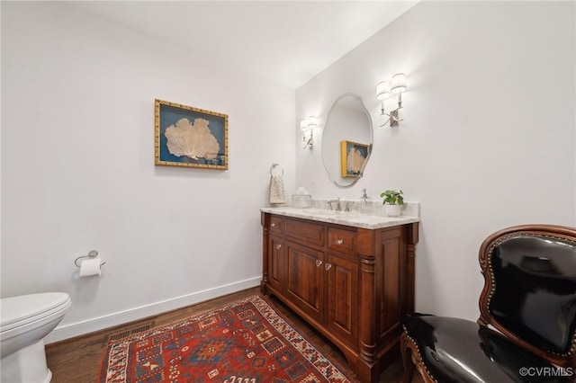 bathroom featuring toilet, baseboards, wood finished floors, and vanity