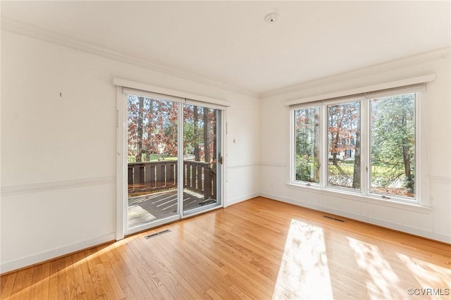 empty room featuring crown molding, light hardwood / wood-style flooring, and a wealth of natural light