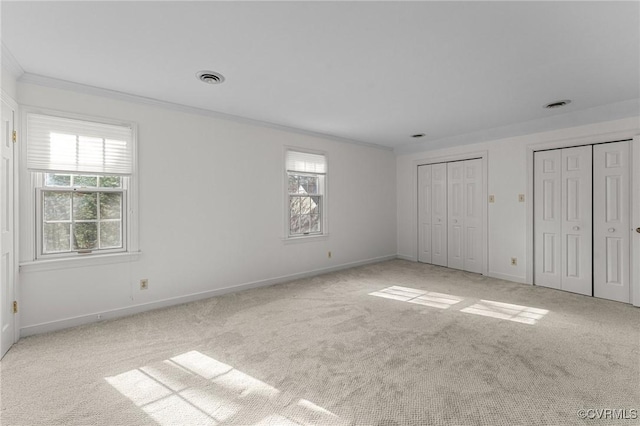 unfurnished bedroom featuring ornamental molding, two closets, and light colored carpet