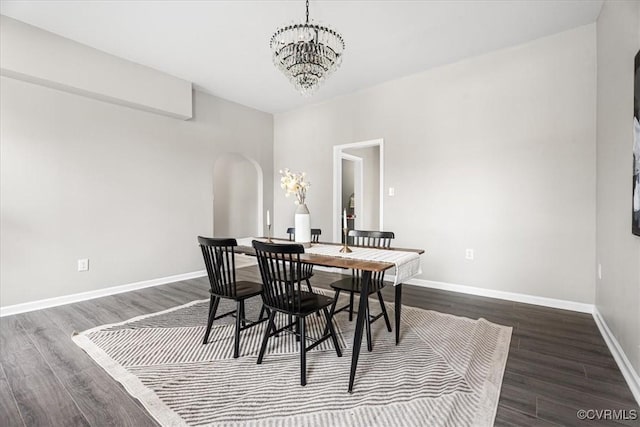 dining space with arched walkways, an inviting chandelier, wood finished floors, and baseboards