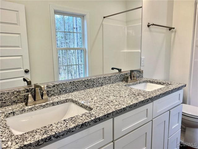 bathroom featuring double vanity, a sink, toilet, and walk in shower