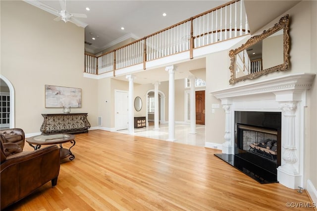 living room with ornate columns, wood-type flooring, a high ceiling, ornamental molding, and ceiling fan