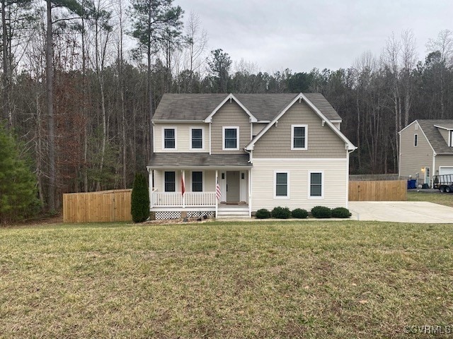 view of front facade featuring covered porch, fence, a wooded view, and a front yard