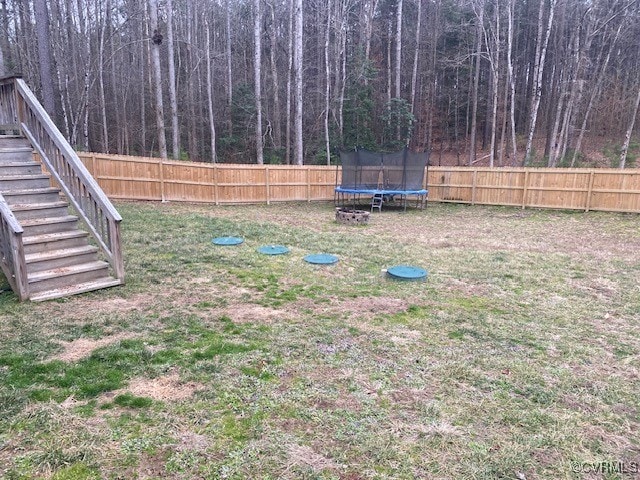 view of yard featuring stairs, a forest view, a trampoline, and a fenced backyard