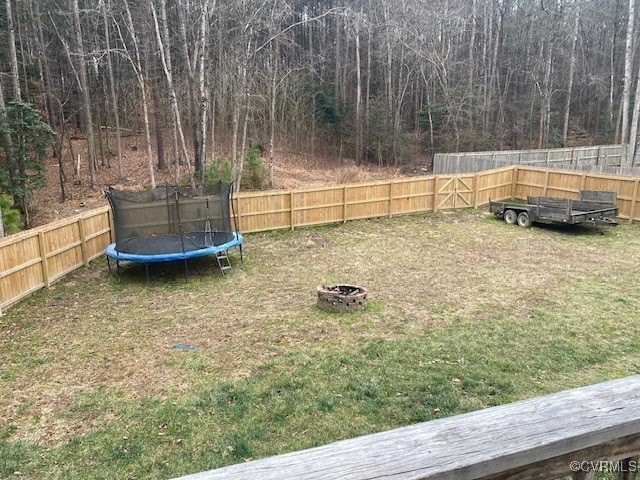 view of yard with a trampoline, an outdoor fire pit, and a fenced backyard