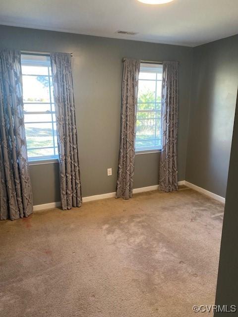 empty room featuring carpet floors, a healthy amount of sunlight, visible vents, and baseboards