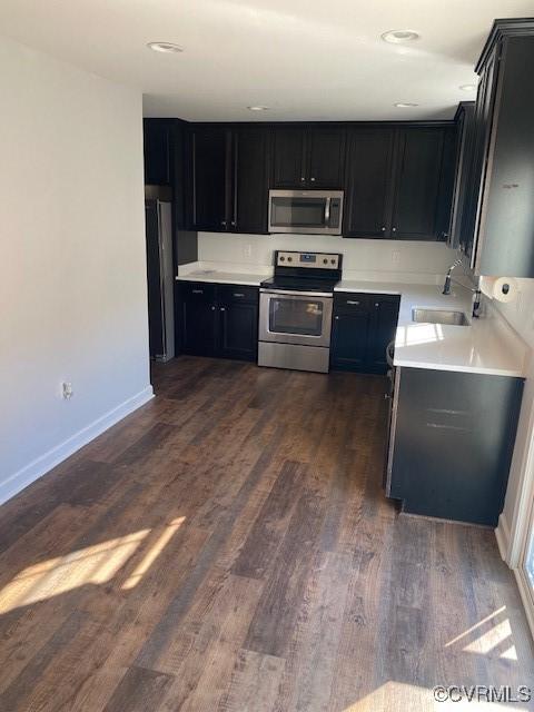 kitchen with dark wood finished floors, dark cabinetry, stainless steel appliances, and a sink