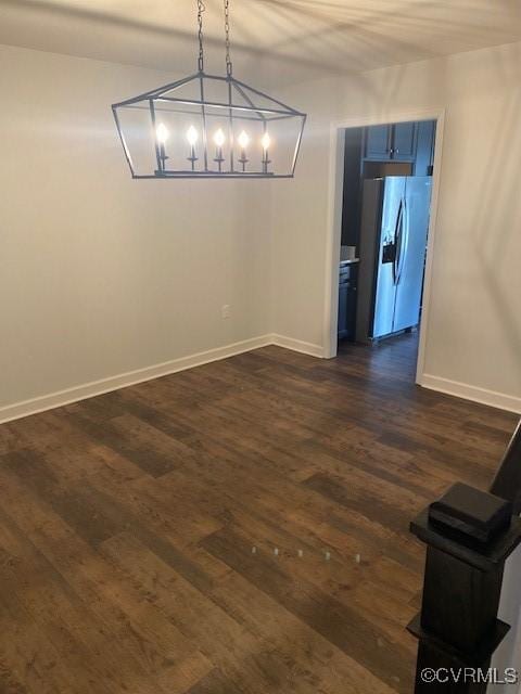 unfurnished dining area featuring an inviting chandelier, baseboards, and dark wood finished floors