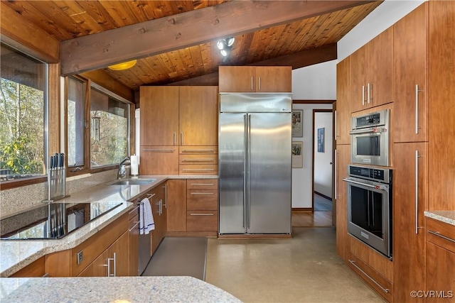 kitchen with black electric stovetop, stainless steel built in fridge, sink, and light stone countertops