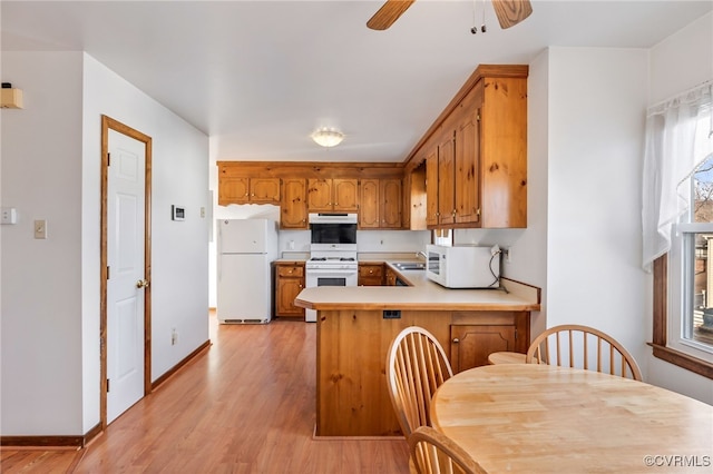 kitchen with white appliances, light hardwood / wood-style flooring, kitchen peninsula, and a healthy amount of sunlight