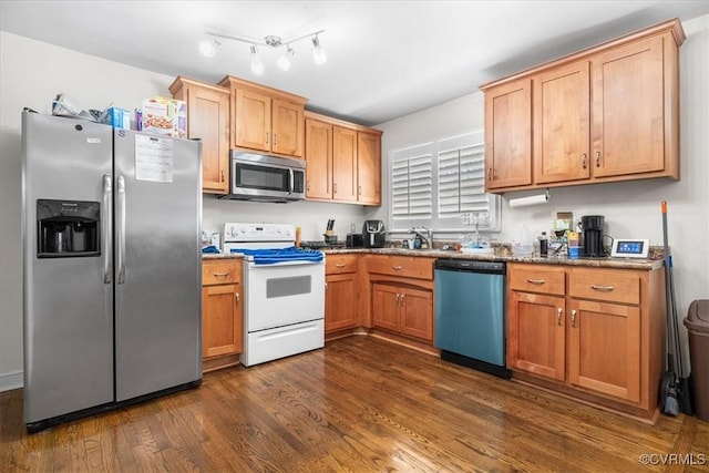 kitchen featuring appliances with stainless steel finishes, dark wood-type flooring, sink, and dark stone counters