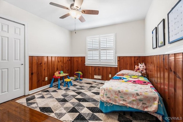 bedroom with hardwood / wood-style flooring, ceiling fan, and wood walls