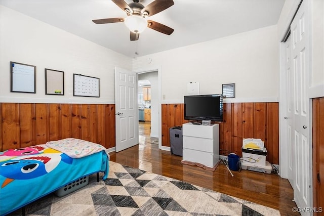 bedroom with dark wood-type flooring, ceiling fan, a closet, and wood walls