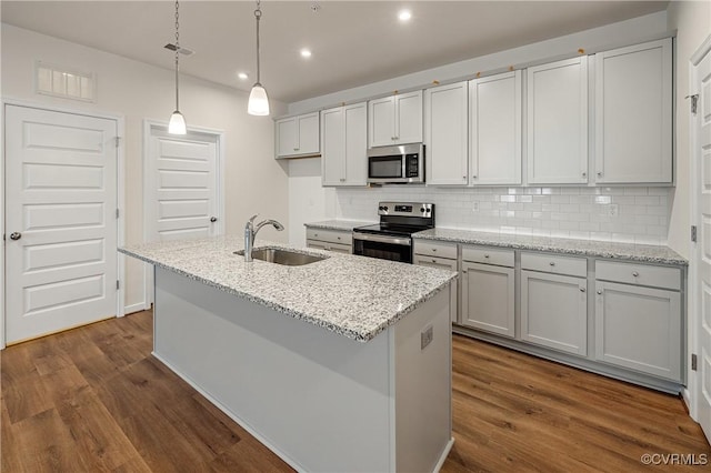 kitchen featuring pendant lighting, sink, appliances with stainless steel finishes, light stone counters, and a center island with sink