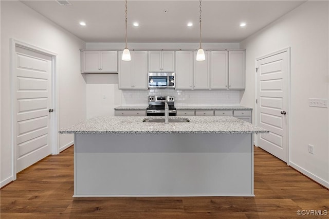 kitchen featuring sink, appliances with stainless steel finishes, a kitchen island with sink, hanging light fixtures, and light stone countertops