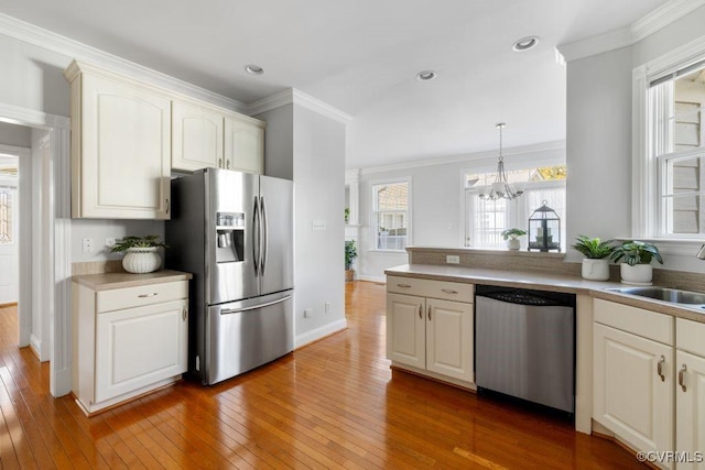 kitchen with crown molding, appliances with stainless steel finishes, sink, and hanging light fixtures