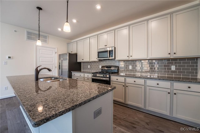 kitchen featuring appliances with stainless steel finishes, sink, dark stone countertops, white cabinets, and a center island with sink