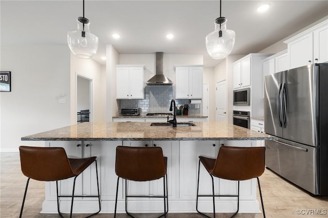 kitchen featuring appliances with stainless steel finishes, an island with sink, and wall chimney range hood