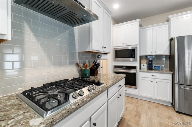 kitchen featuring appliances with stainless steel finishes, light stone counters, light hardwood / wood-style floors, white cabinets, and wall chimney exhaust hood