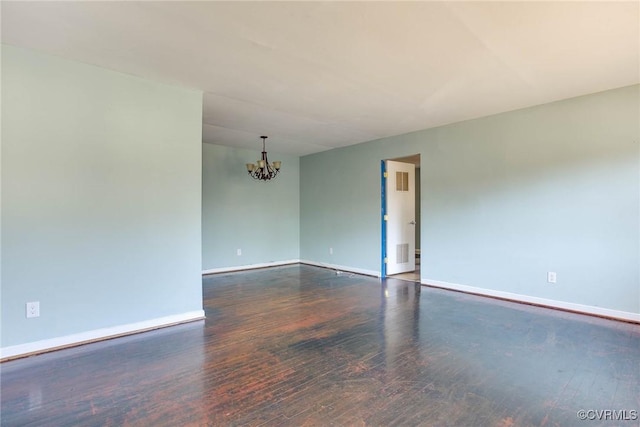 empty room featuring dark wood-type flooring and a notable chandelier