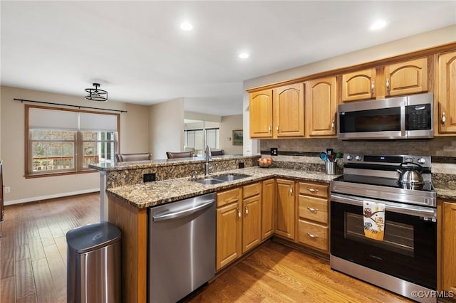 kitchen with stainless steel appliances, sink, stone counters, and kitchen peninsula