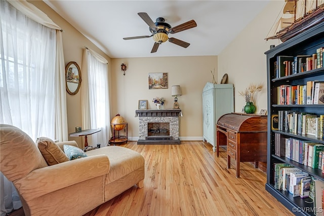 living area featuring a stone fireplace, light hardwood / wood-style floors, and ceiling fan