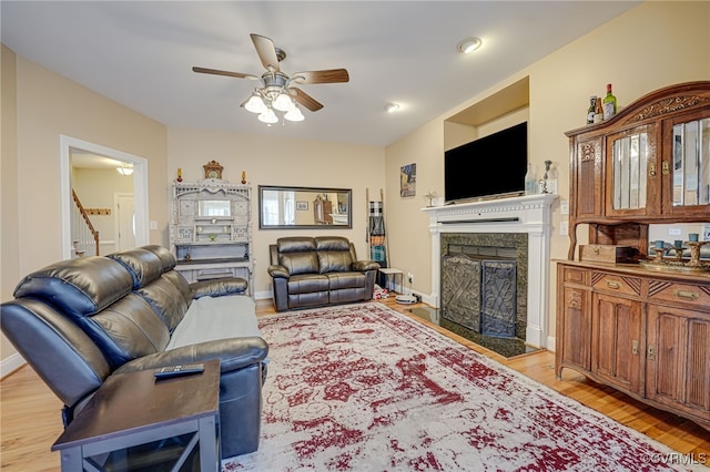 living room featuring a high end fireplace, ceiling fan, and light wood-type flooring