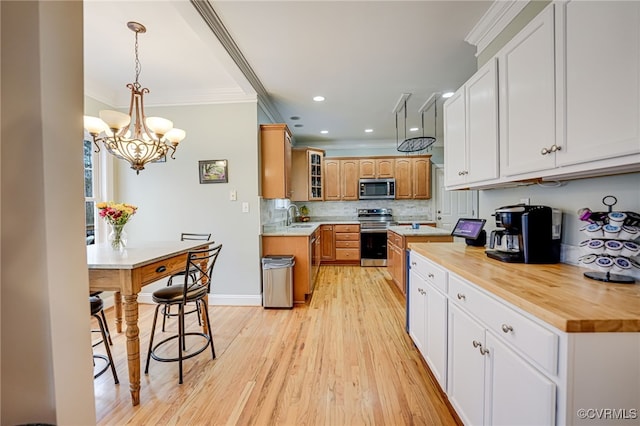 kitchen with sink, wooden counters, backsplash, stainless steel appliances, and decorative light fixtures